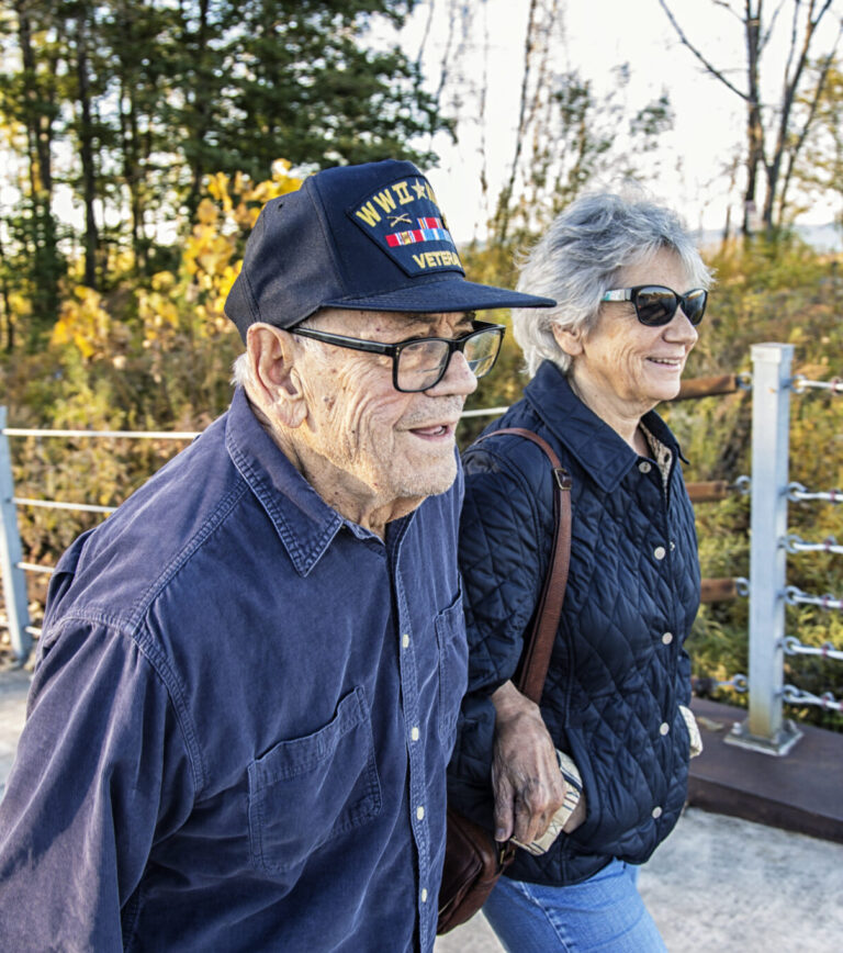 A proud, elderly, 93 year old real person senior adult man USA WWII and Korean Conflict military war veteran and his real life senior adult woman home caregiver daughter are walking side by side sightseeing on a sunny day at a public park on the shoreline of Lake Ontario. He is wearing a common, unbranded, generic souvenir shop military veteran commemorative baseball style cap with generic wording, replica plastic insignia pins and replica campaign ribbon iron-on patches. Photo taken near Rochester, N.Y., in the Finger Lakes region of western New York State, USA.

NOTE: There are no official or authentic military uniform elements and no intent to portray anything other than a patriotic United States military veteran.